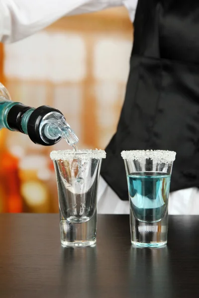 Barmen hand with bottle pouring beverage into glasses, on bright background — Stock Photo, Image