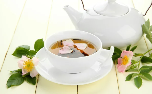 Taza y tetera de té de hierbas con flores de rosa de la cadera en la mesa de madera blanca — Foto de Stock