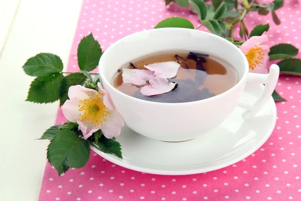 Kopje kruidenthee met hip roze bloemen op witte houten tafel — Stockfoto