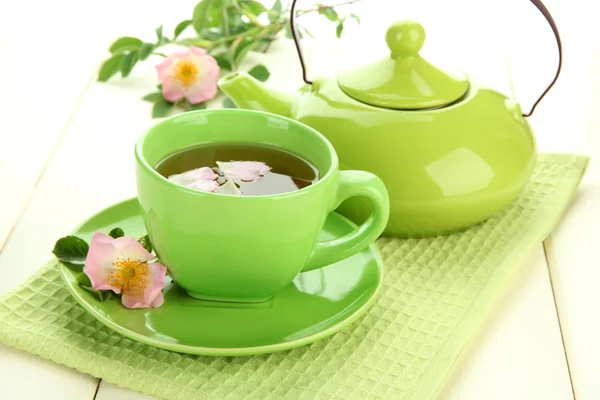 Taza y tetera de té de hierbas con flores de rosa de la cadera en la mesa de madera blanca — Foto de Stock