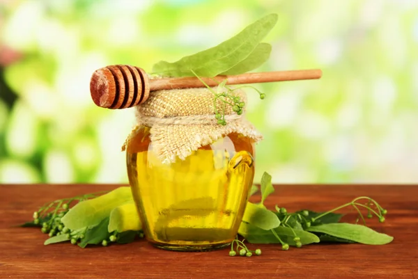 Jar of honey with flowers of lime, on wooden table on bright background — Stock Photo, Image