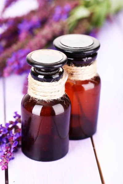 Медицинские бутылки и цветы сальвии на фиолетовом деревянном фоне — стоковое фото