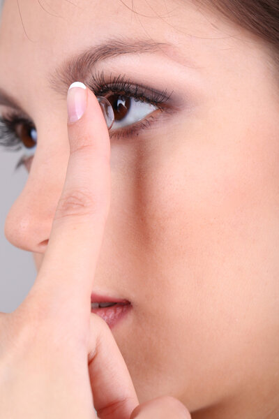 Young woman putting contact lens in her eye close up