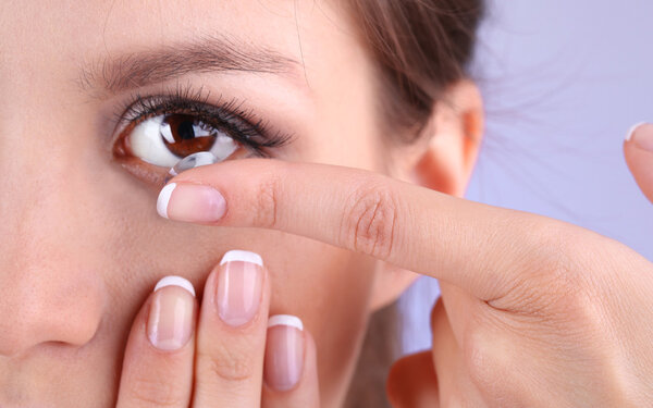 Young woman putting contact lens in her eye close up