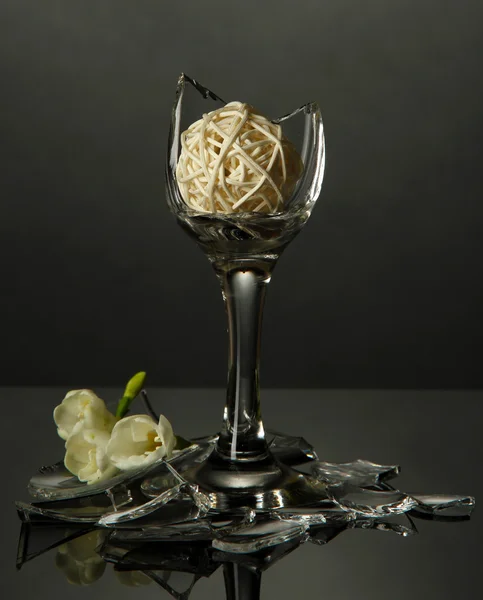 Broken wineglass with flower on grey background — Stock Photo, Image