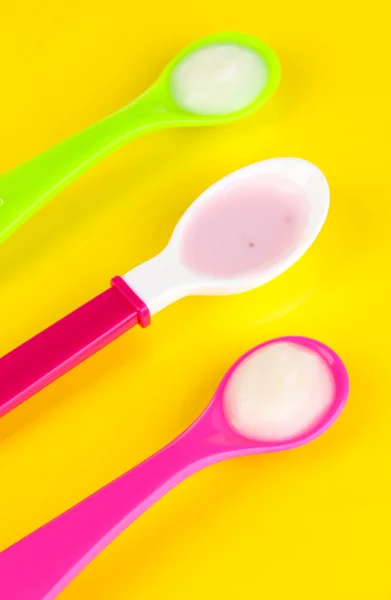 Color spoons for baby food on yellow background — Stock Photo, Image
