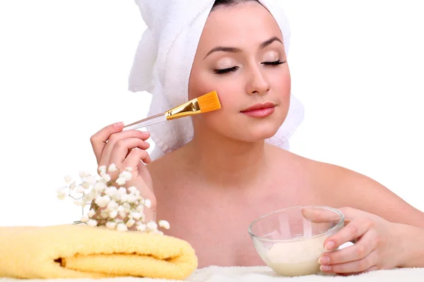 Belle jeune femme avec crème pour masque facial et serviette sur sa tête isolée sur blanc — Photo