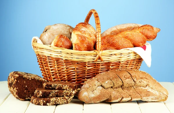 Состав с хлебом и рулонами, в плетеной корзине на деревянном столе, на цветном фоне — стоковое фото