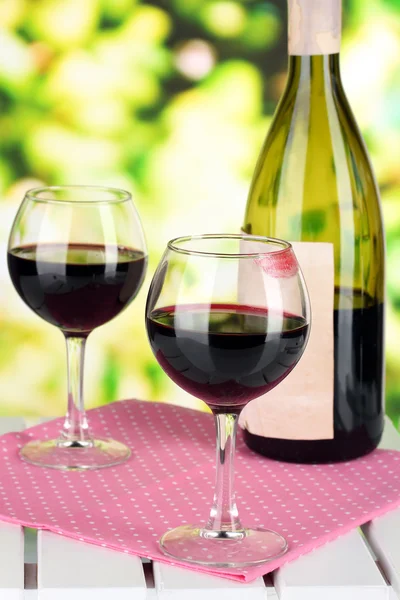 Two glasses of wine and bottle on table on nature background — Stock Photo, Image