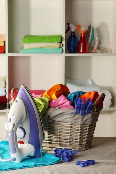 Ropa y plancha en la mesa sobre los estantes de fondo — Foto de Stock