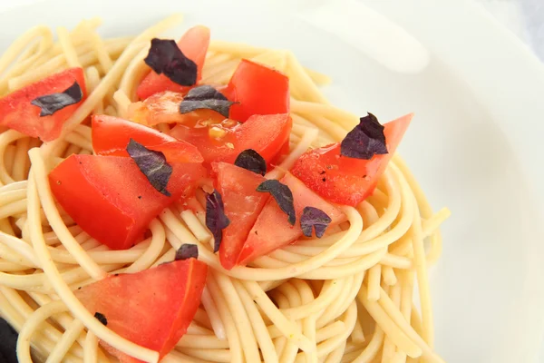 Espaguete com tomates e folhas de manjericão close-up — Fotografia de Stock