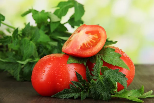 Fresh tomatoes and young plant on wooden table on natural background — Stock Photo, Image