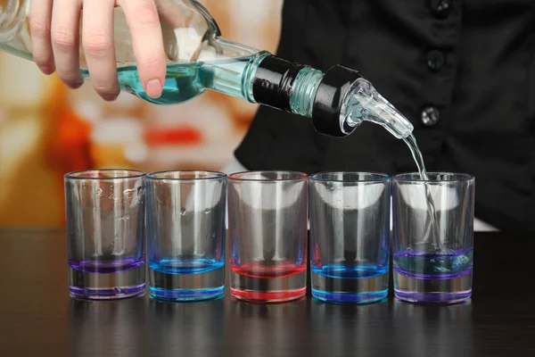 Barmen hand with bottle pouring beverage into glasses, on bright background — Stock Photo, Image