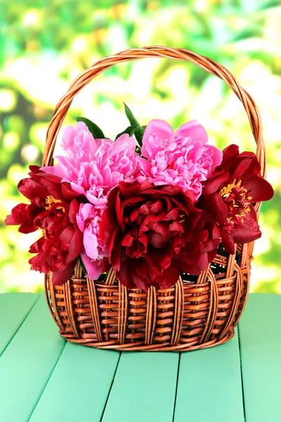 Piękne piwonie w wiklinowym koszu na stole na jasnym tle — Zdjęcie stockowe