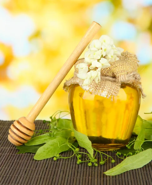 Tarro de miel con flores de lima, sobre estera de bambú de color sobre fondo brillante — Foto de Stock