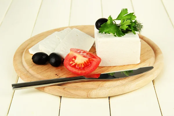 Queso de leche de oveja, aceitunas negras, tomate rojo con perejil y eneldo en tabla de cortar, sobre fondo de madera de color —  Fotos de Stock