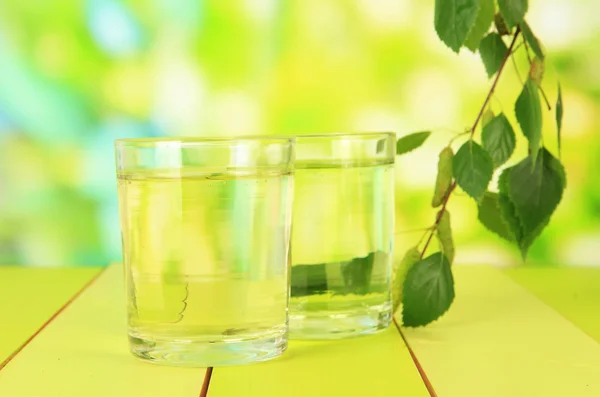 Glasses of birch sap on wooden table, on green background — Stock Photo, Image