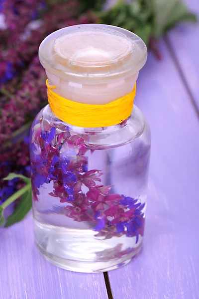 Medizinflasche mit Salvia-Blüten auf violettem Holzhintergrund — Stockfoto