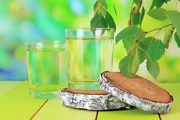 Glasses of birch sap on wooden table, on green background — Stock Image Glasses of birch sap on wooden table, on green background Royalty Free Stock Photos