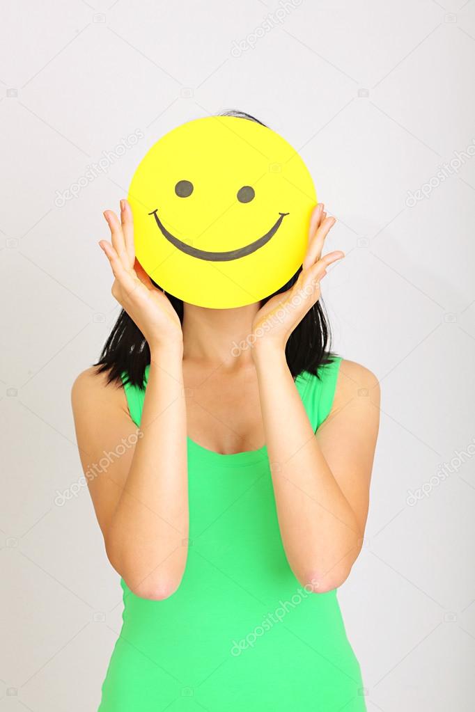 Young woman holding paper with happy smiley on gray background.