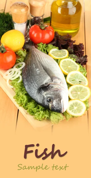 Fresh dorado on chopping board with lemon and vegetables on wooden table — Stock Photo, Image