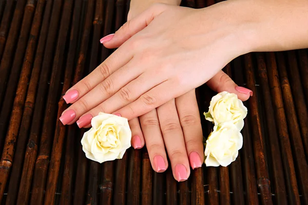 Manos de mujer con manicura rosa y flores, sobre fondo de estera de bambú —  Fotos de Stock