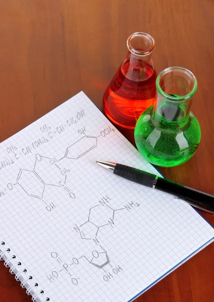 Reagenzgläser mit bunten Flüssigkeiten und Formeln auf dem Tisch — Stockfoto