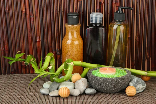 Still life with green bamboo plant and stones, on bamboo mat on color background — Stock Photo, Image