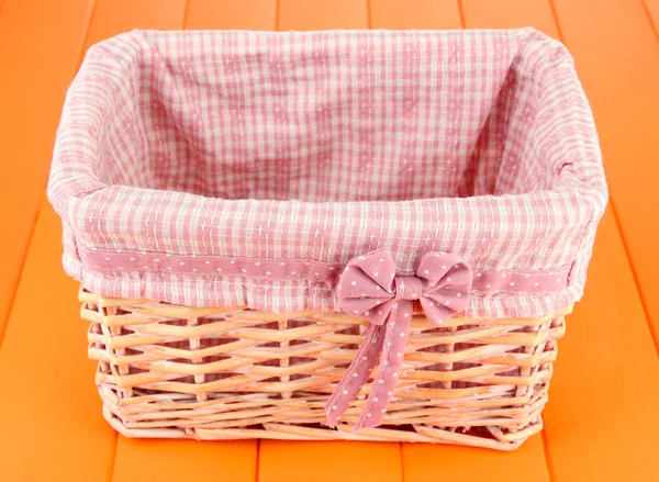 Wicket basket with pink fabric and bow, on color wooden background — Stock Photo, Image