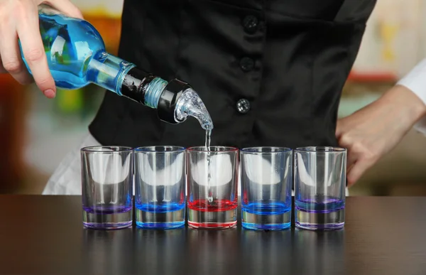 Barmen mão com garrafa derramando bebida em copos, no fundo brilhante — Fotografia de Stock