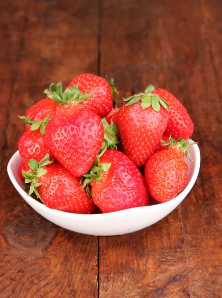 Verse aardbeien in kom op houten achtergrond — Stockfoto