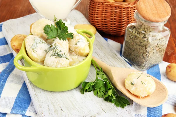 Tender young potatoes with sour cream and herbs in pan on wooden board on table close-up — Stock Photo, Image