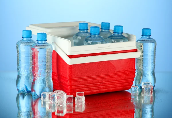 Reisekühlschrank mit Wasserflaschen und Eiswürfeln, auf blauem Hintergrund — Stockfoto