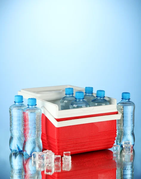 Refrigerador viajero con botellas de agua y cubitos de hielo, sobre fondo azul —  Fotos de Stock