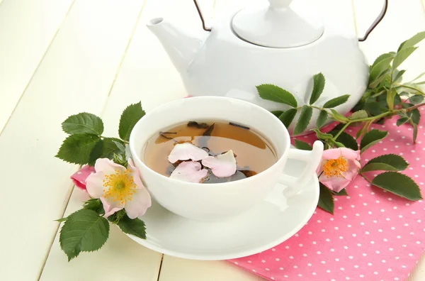 Cup en theepot van kruiden thee met hip roze bloemen op witte houten tafel — Stockfoto