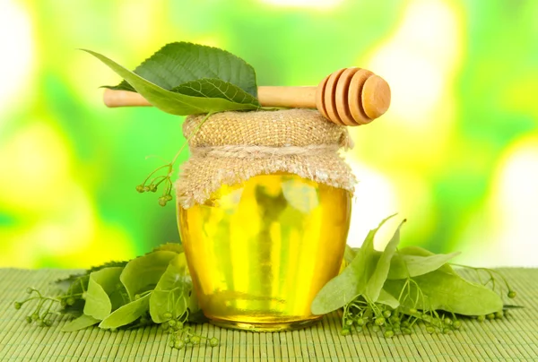 Jar of honey with flowers of lime, on color bamboo mat on bright background — Stock Photo, Image