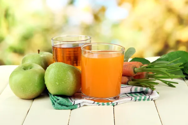 Bicchieri di succo, mele e carote su tavolo di legno bianco, su sfondo verde — Foto Stock