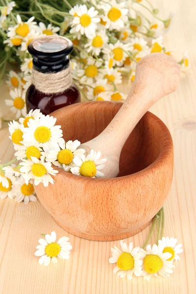 Aceite esencial y flores de manzanilla en mortero sobre mesa de madera —  Fotos de Stock