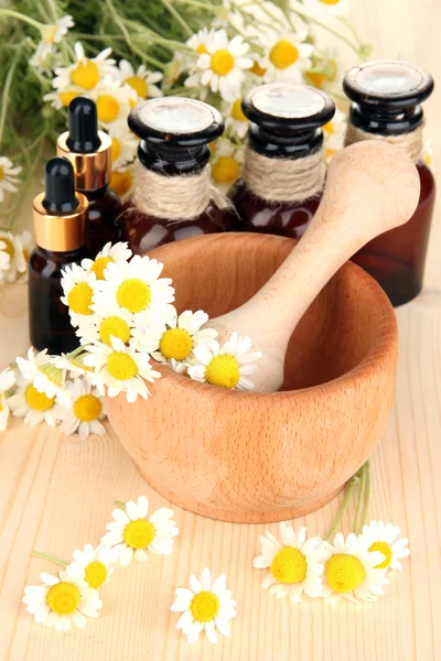 Aceite esencial y flores de manzanilla en mortero sobre mesa de madera —  Fotos de Stock