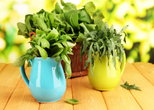 Fresh herbs in pitchers and basket on wooden table on natural background — Stock Photo, Image