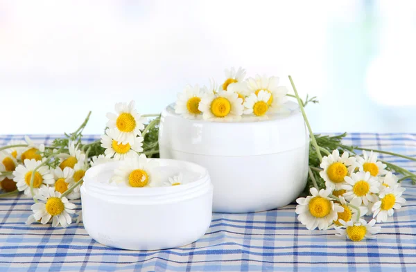 Cream with chamomile on checkered cloth on room background — Stock Photo, Image