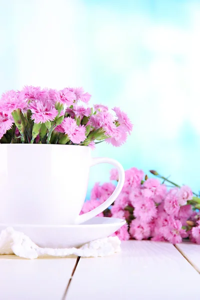 Mnoho malých pink hřebíček v poháru na dřevěný stůl na pozadí okna — Stock fotografie