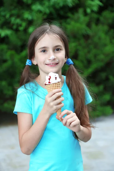 Маленькая девочка катается на коньках есть вкусное мороженое на фоне парка — стоковое фото