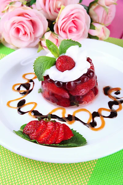 Sabroso postre de gelatina con bayas frescas, sobre fondo de rosas rosadas — Foto de Stock