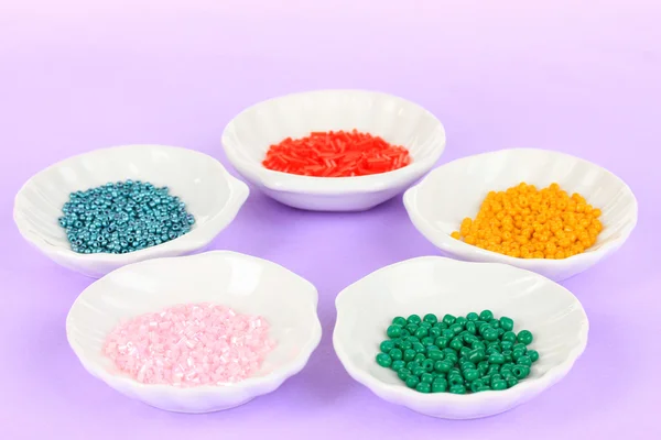 Diverse perline colorate su piatti su sfondo viola — Foto Stock