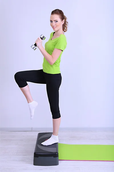 Belos exercícios de mulher jovem com halteres no stepper — Fotografia de Stock