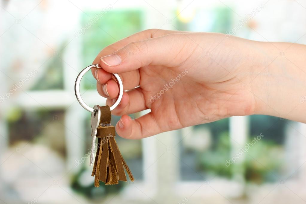 Key with leather trinket in hand on window background