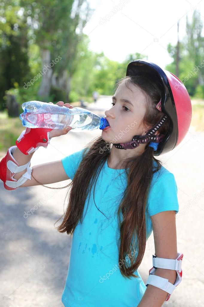Little girl in roller skates drinking water at park