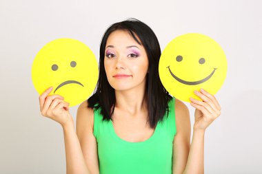 mutlu ve üzgün smiley ile kağıt gri arka plan üzerinde tutan genç kadın
