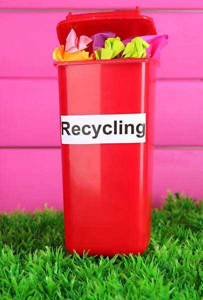 Recycling bin with papers on grass on pink background — Stock Photo, Image